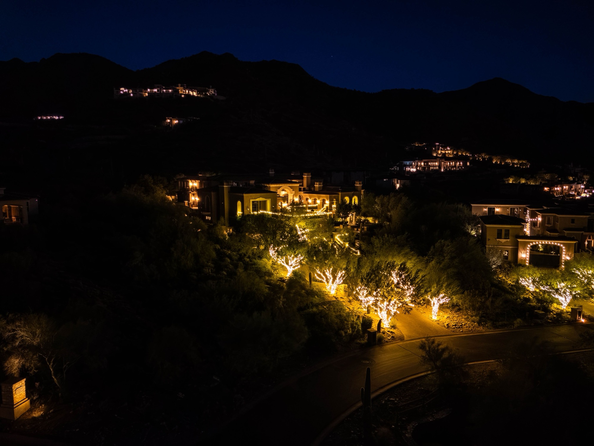 Wide aerial view of a fully lit Grayhawk hillside estate